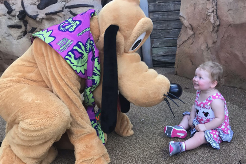 Pluto bending down to thrill a baby girl.